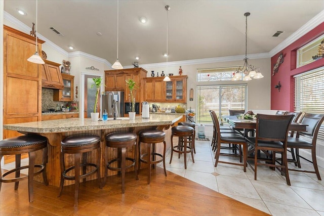 kitchen featuring visible vents, brown cabinetry, decorative backsplash, glass insert cabinets, and freestanding refrigerator