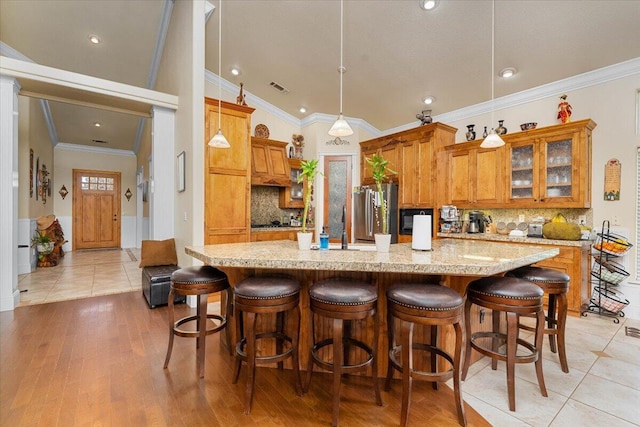 kitchen featuring black microwave, visible vents, freestanding refrigerator, brown cabinetry, and a large island with sink