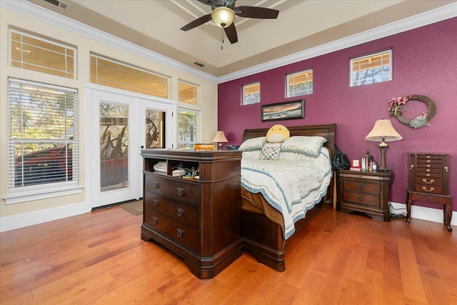 bedroom with light wood-style floors, an accent wall, baseboards, and crown molding