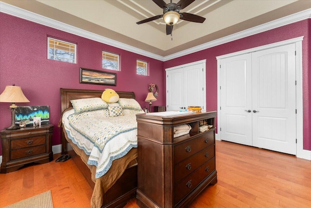 bedroom featuring a tray ceiling, crown molding, light wood finished floors, two closets, and a ceiling fan