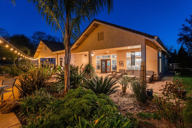 back of house at night with a patio area and stucco siding