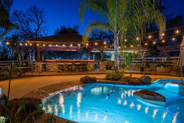 pool at twilight with outdoor dry bar, a gazebo, a patio, and an outdoor pool