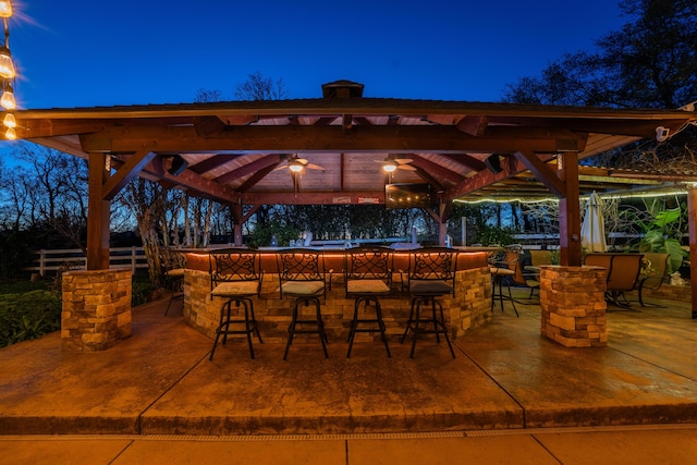 patio at twilight featuring fence, outdoor dry bar, and a gazebo