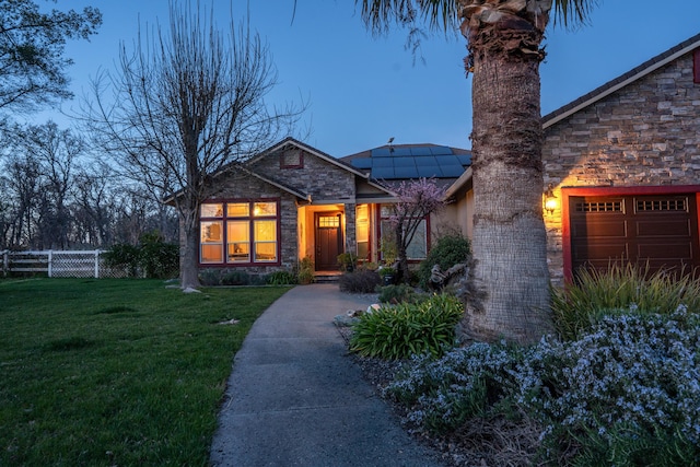 view of front of home with a garage, stone siding, fence, roof mounted solar panels, and a front yard