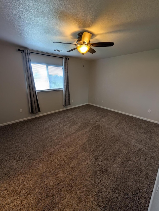 empty room featuring dark colored carpet, ceiling fan, a textured ceiling, and baseboards