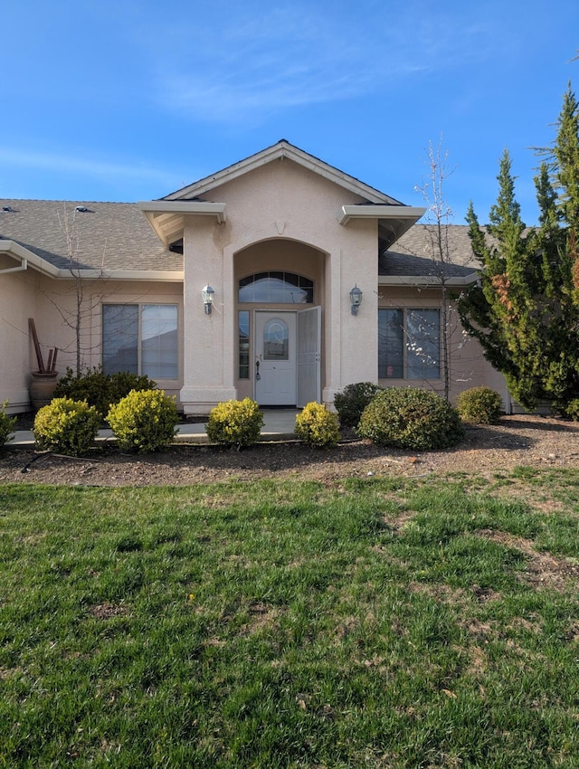 doorway to property with a yard, roof with shingles, and stucco siding