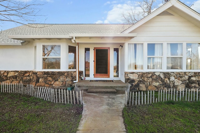 view of exterior entry featuring a shingled roof, stone siding, and fence