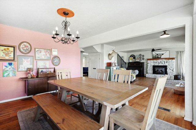 dining room with baseboards, visible vents, a fireplace with raised hearth, stairway, and wood finished floors