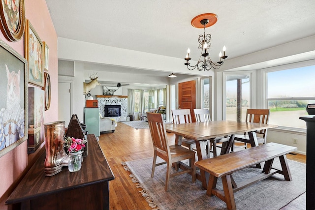 dining space featuring ceiling fan with notable chandelier, a fireplace, and wood finished floors