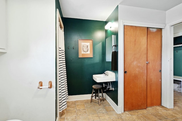 bathroom with a stall shower, stone finish floor, a sink, and baseboards