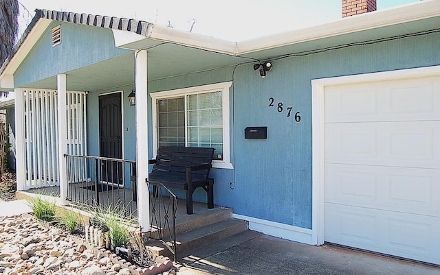 entrance to property with a garage, a chimney, and a porch