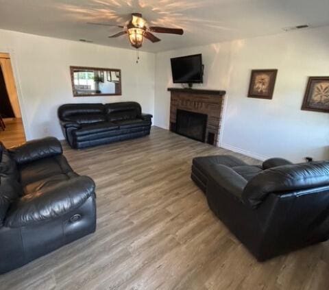 living area featuring a brick fireplace, visible vents, a ceiling fan, and wood finished floors