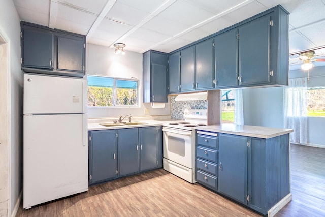 kitchen featuring white appliances, range hood, a peninsula, a sink, and blue cabinets