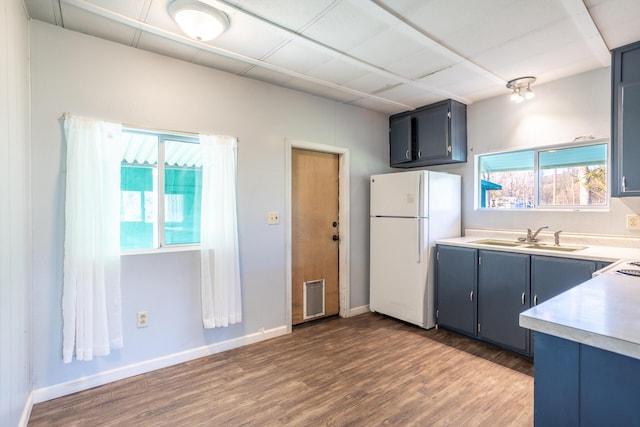 kitchen featuring wood finished floors, blue cabinetry, freestanding refrigerator, a sink, and light countertops