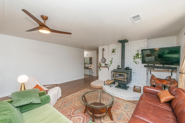 living room featuring a textured ceiling, wood finished floors, visible vents, a ceiling fan, and a wood stove