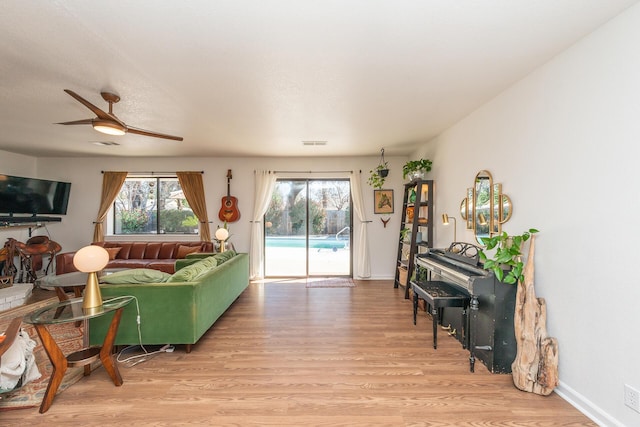 living area with ceiling fan, light wood finished floors, visible vents, and baseboards