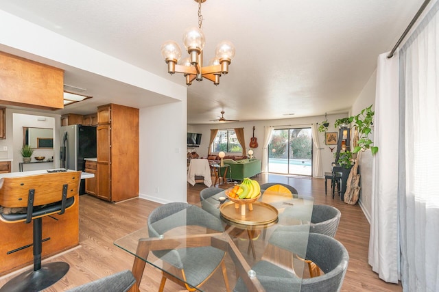 dining room featuring light wood finished floors, baseboards, and ceiling fan with notable chandelier