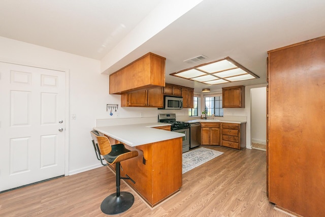 kitchen with brown cabinets, light wood-type flooring, visible vents, and stainless steel appliances