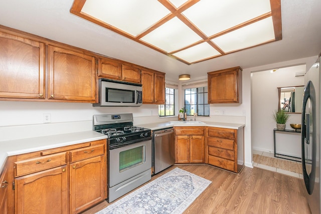 kitchen with stainless steel appliances, brown cabinetry, light countertops, and a sink