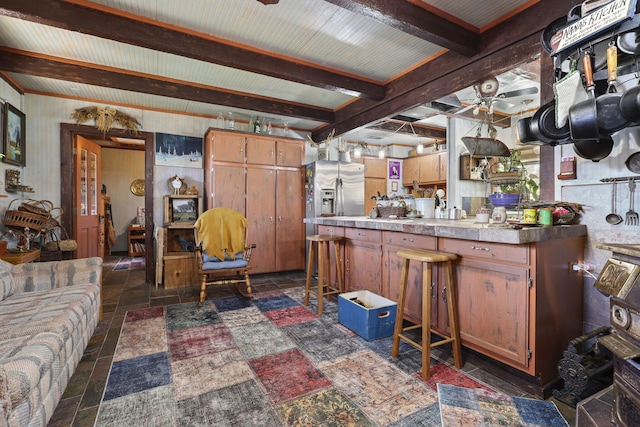 kitchen with ceiling fan, stone tile floors, a peninsula, stainless steel refrigerator with ice dispenser, and beam ceiling