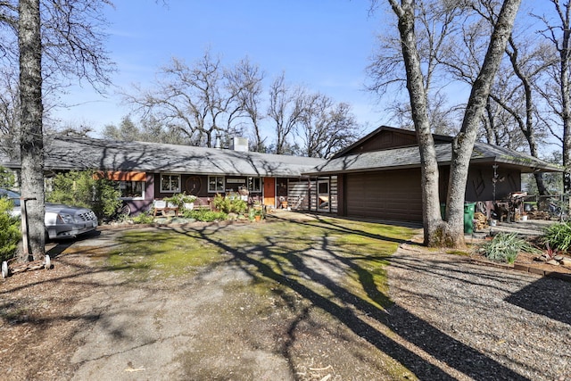 view of front facade with an attached garage, a chimney, and dirt driveway