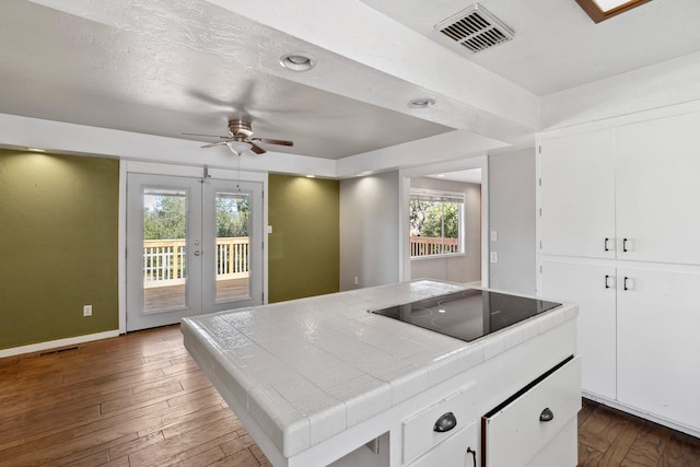 kitchen featuring visible vents, black electric stovetop, dark wood-style floors, and tile counters