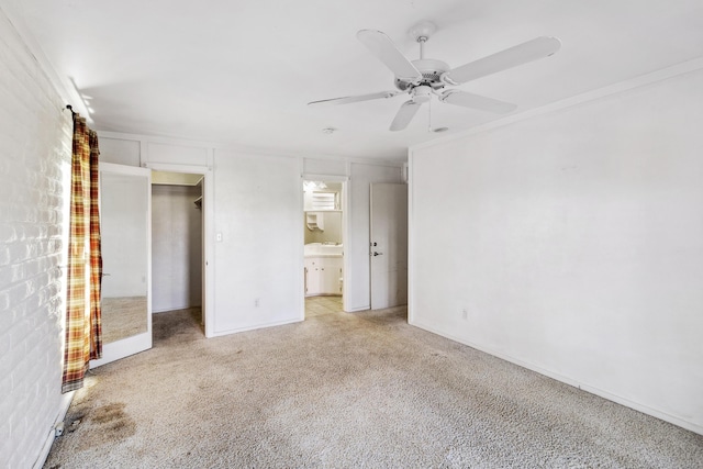 unfurnished bedroom featuring a ceiling fan, light colored carpet, ensuite bath, ornamental molding, and a walk in closet