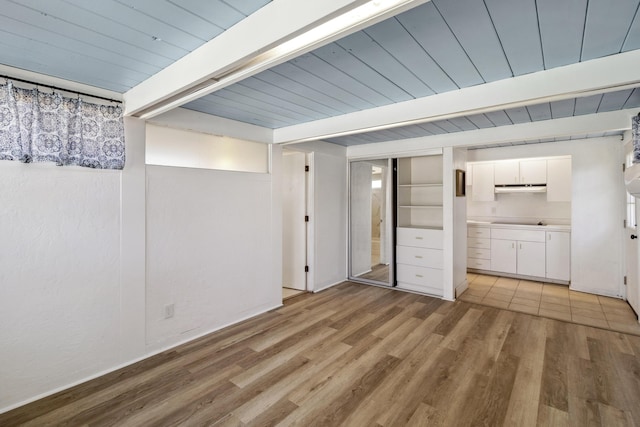 unfurnished bedroom featuring light wood-style flooring, ensuite bath, and beam ceiling