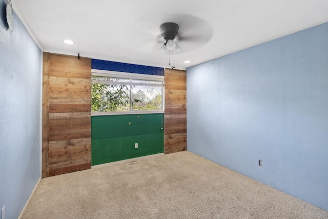 carpeted spare room with a ceiling fan, recessed lighting, visible vents, and wood walls