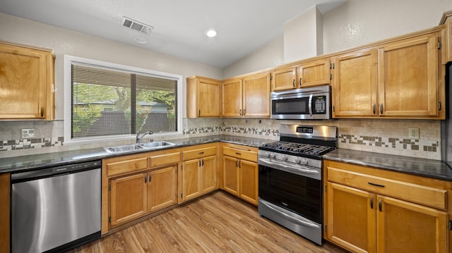 kitchen with light wood-type flooring, vaulted ceiling, visible vents, appliances with stainless steel finishes, and a sink