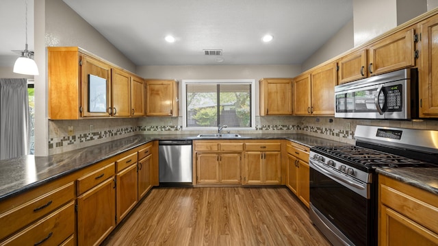 kitchen featuring dark countertops, visible vents, appliances with stainless steel finishes, light wood finished floors, and a sink