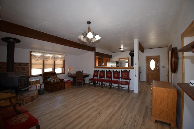 living room featuring beamed ceiling, a wood stove, a textured ceiling, light wood-type flooring, and a notable chandelier