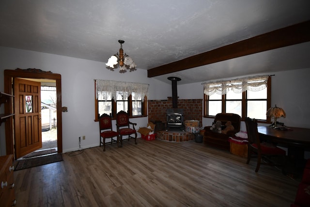 living area featuring a wood stove, a textured ceiling, wood finished floors, a chandelier, and beamed ceiling