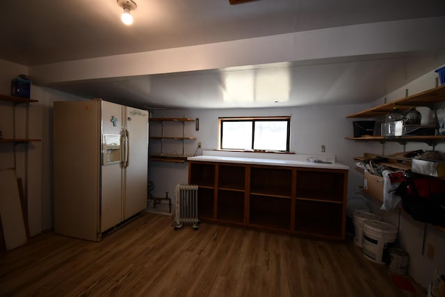 below grade area with radiator heating unit, white fridge with ice dispenser, and wood finished floors