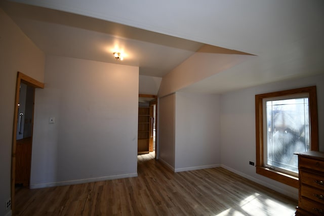 empty room featuring baseboards, vaulted ceiling, and wood finished floors