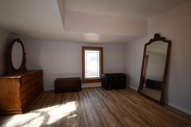 unfurnished bedroom featuring lofted ceiling, baseboards, and wood finished floors