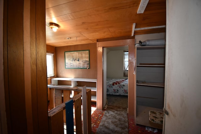 hallway with wooden ceiling, carpet, and an upstairs landing