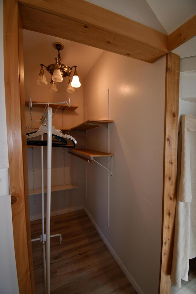 spacious closet with vaulted ceiling, wood finished floors, and an inviting chandelier