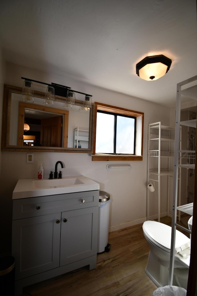 bathroom featuring toilet, wood finished floors, vanity, baseboards, and walk in shower