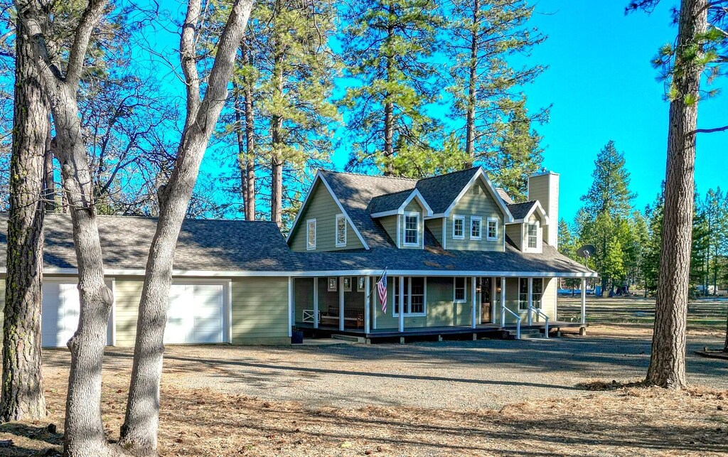 farmhouse-style home featuring roof with shingles, an attached garage, covered porch, a chimney, and dirt driveway