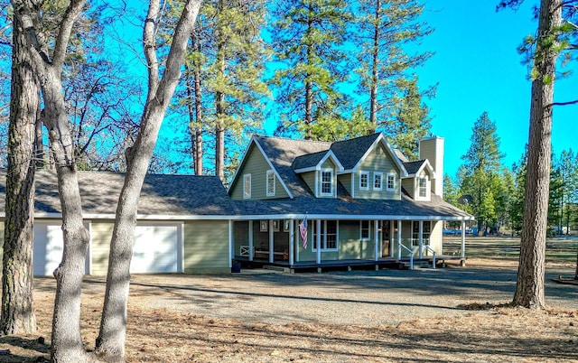 farmhouse-style home featuring roof with shingles, an attached garage, covered porch, a chimney, and dirt driveway