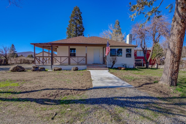 view of front of house featuring covered porch, a front lawn, a chimney, and stucco siding