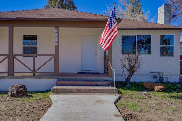 view of front of house with a porch, roof with shingles, a chimney, and stucco siding