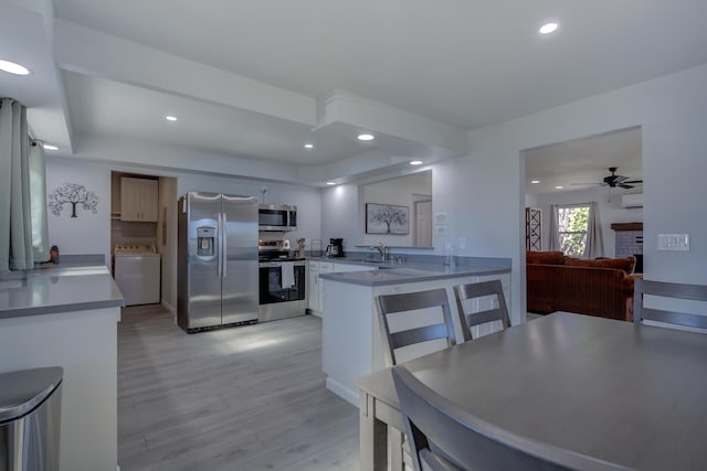 kitchen with stainless steel appliances, a peninsula, washer / clothes dryer, a sink, and light wood finished floors