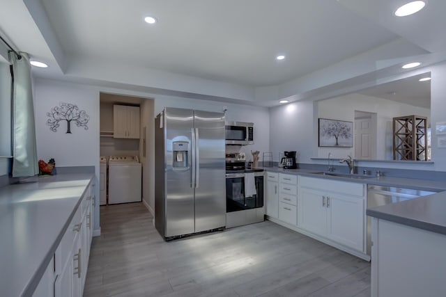 kitchen featuring appliances with stainless steel finishes, washer and clothes dryer, a sink, and white cabinetry