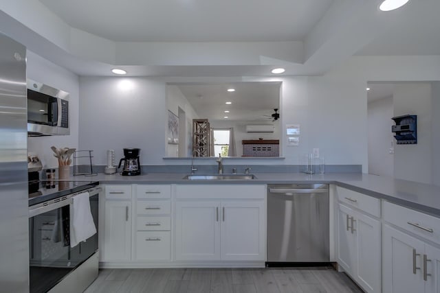 kitchen with white cabinets, a wall unit AC, stainless steel appliances, light wood-type flooring, and a sink