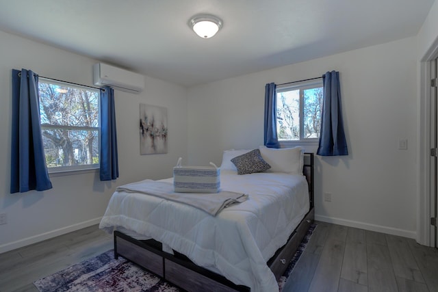 bedroom featuring a wall unit AC, baseboards, and wood finished floors