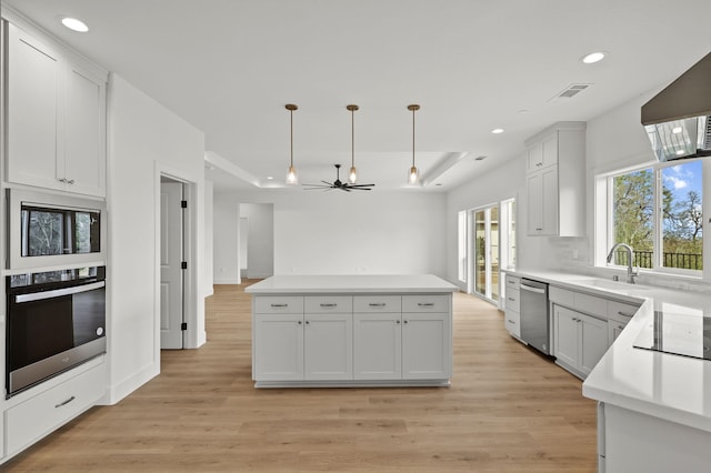 kitchen featuring stainless steel appliances, a sink, visible vents, light wood-style floors, and a tray ceiling