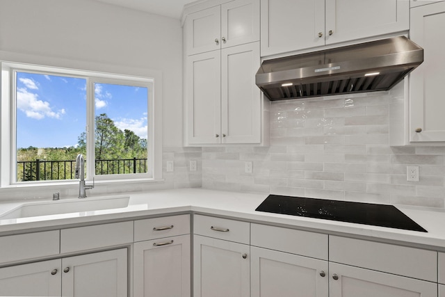 kitchen with backsplash, white cabinets, a sink, under cabinet range hood, and black electric cooktop