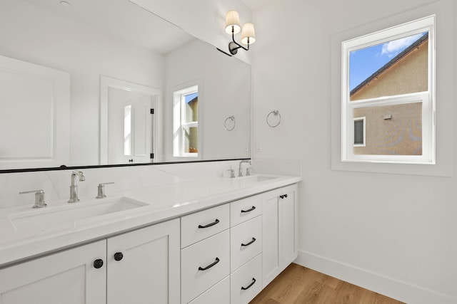 bathroom with double vanity, wood finished floors, a sink, and baseboards